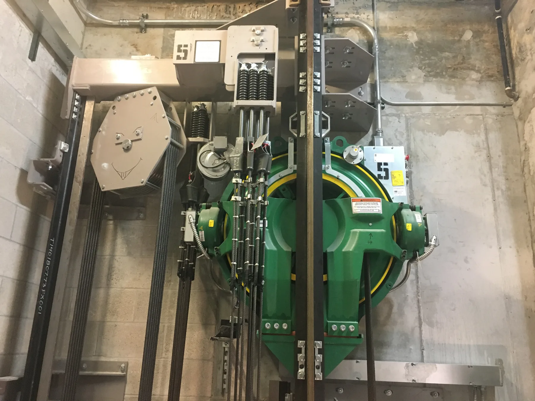 Green elevator machinery and cables inside a concrete machine room