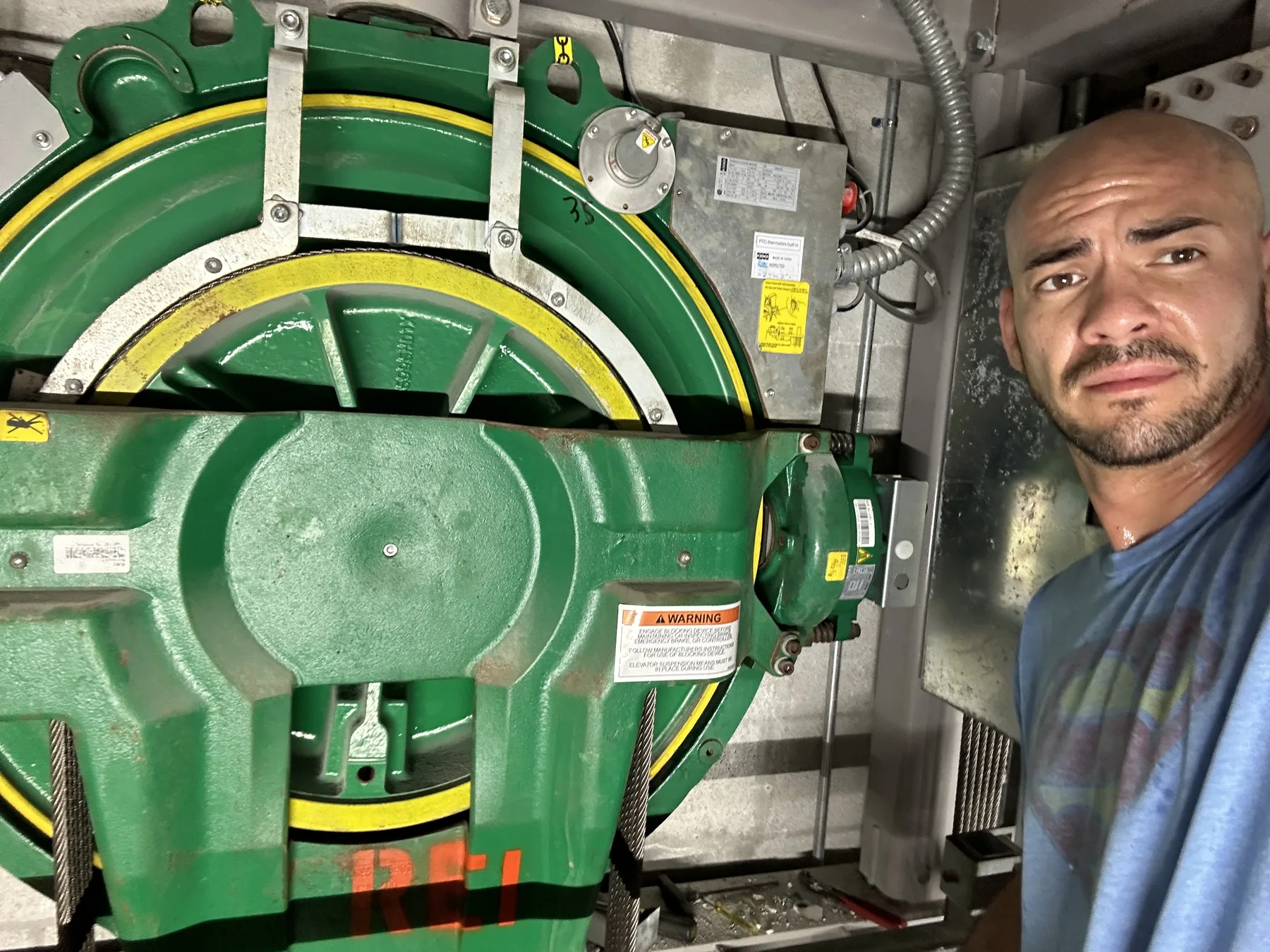 Worker next to a green elevator machine and cables